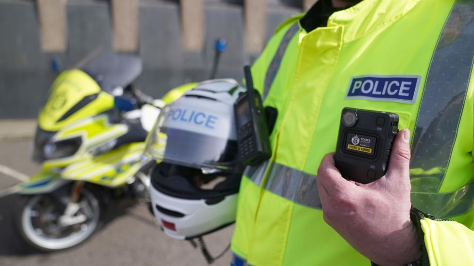 A policeman holding his crash helmet with a motorcycle in the background