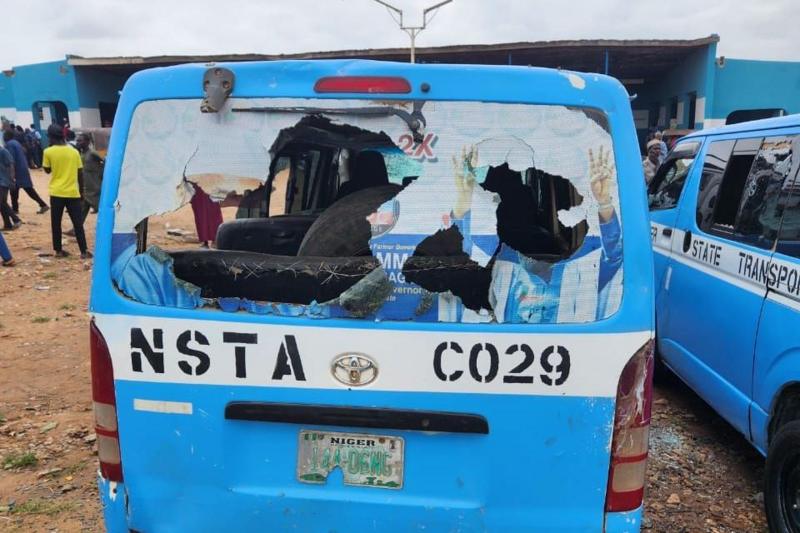 The back of a bus, which has had its windows smashed. It is painted blue and white