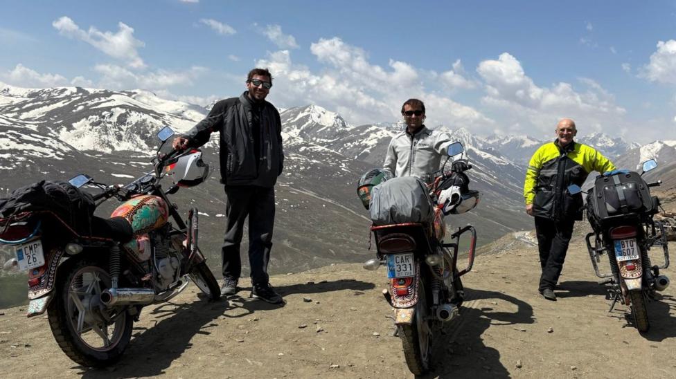 Sean Drysdale and his two sons stand with their motorbikes with snow-capped mountains in the background