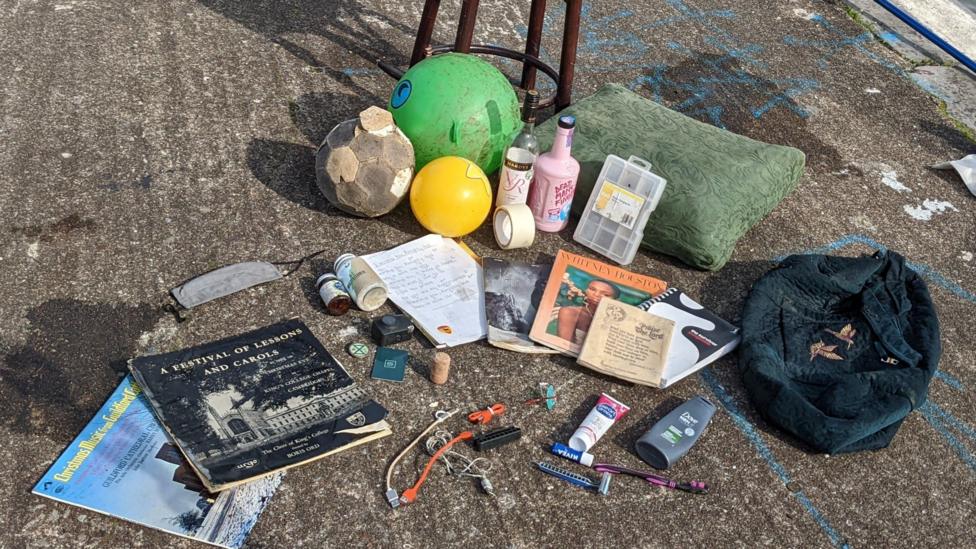 A random assortment of items that have been pulled out from the harbour, including balls, bottles, books, records, toiletries, a bag and a cushion.