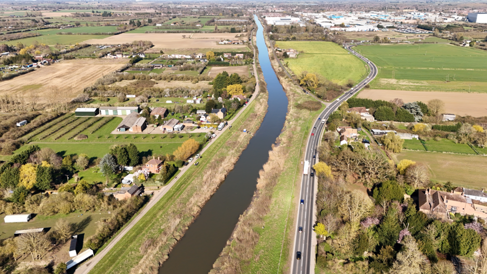 An aerial image of the A47 running next to the river, with North Brink on the other side. The area is mainly rural with a few houses and industrial buildings in clusters.