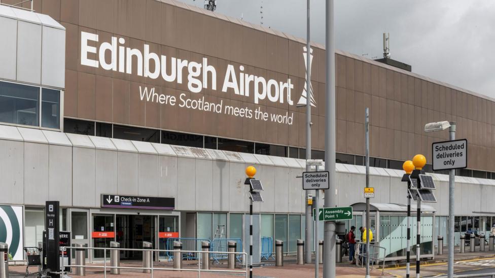 The exterior view of Edinburgh Airport, with a large slogan above the sliding entrance doors saying "where Scotland meets the world" in white letters.