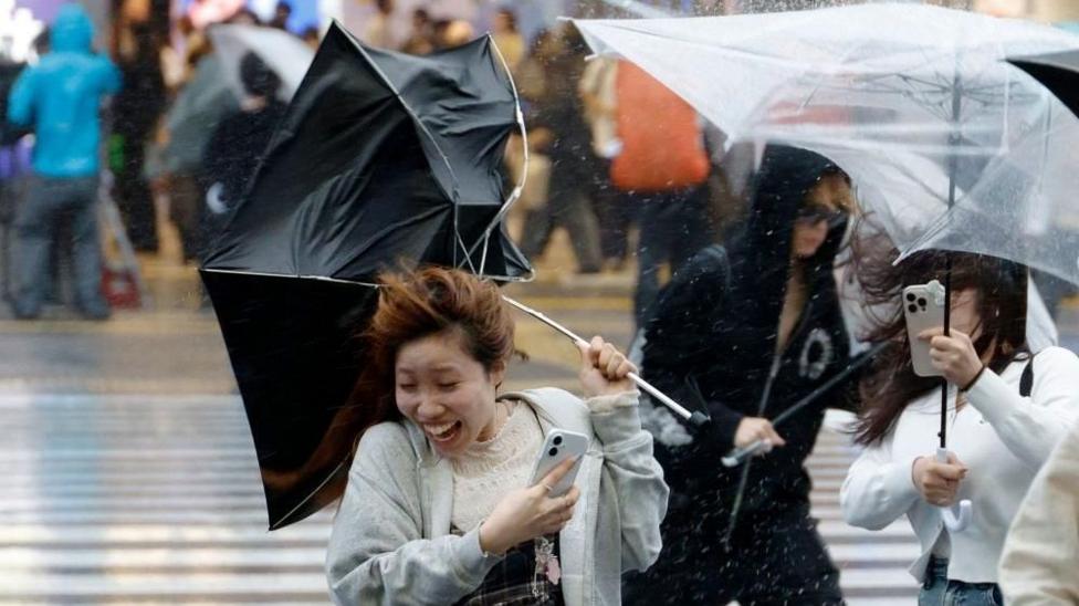 A woman holding an umbrella being blown into the wind.