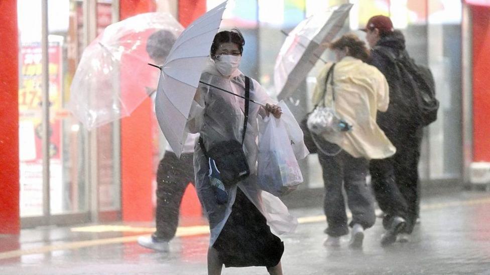 Woman in medical face mask struggling with an umbrella