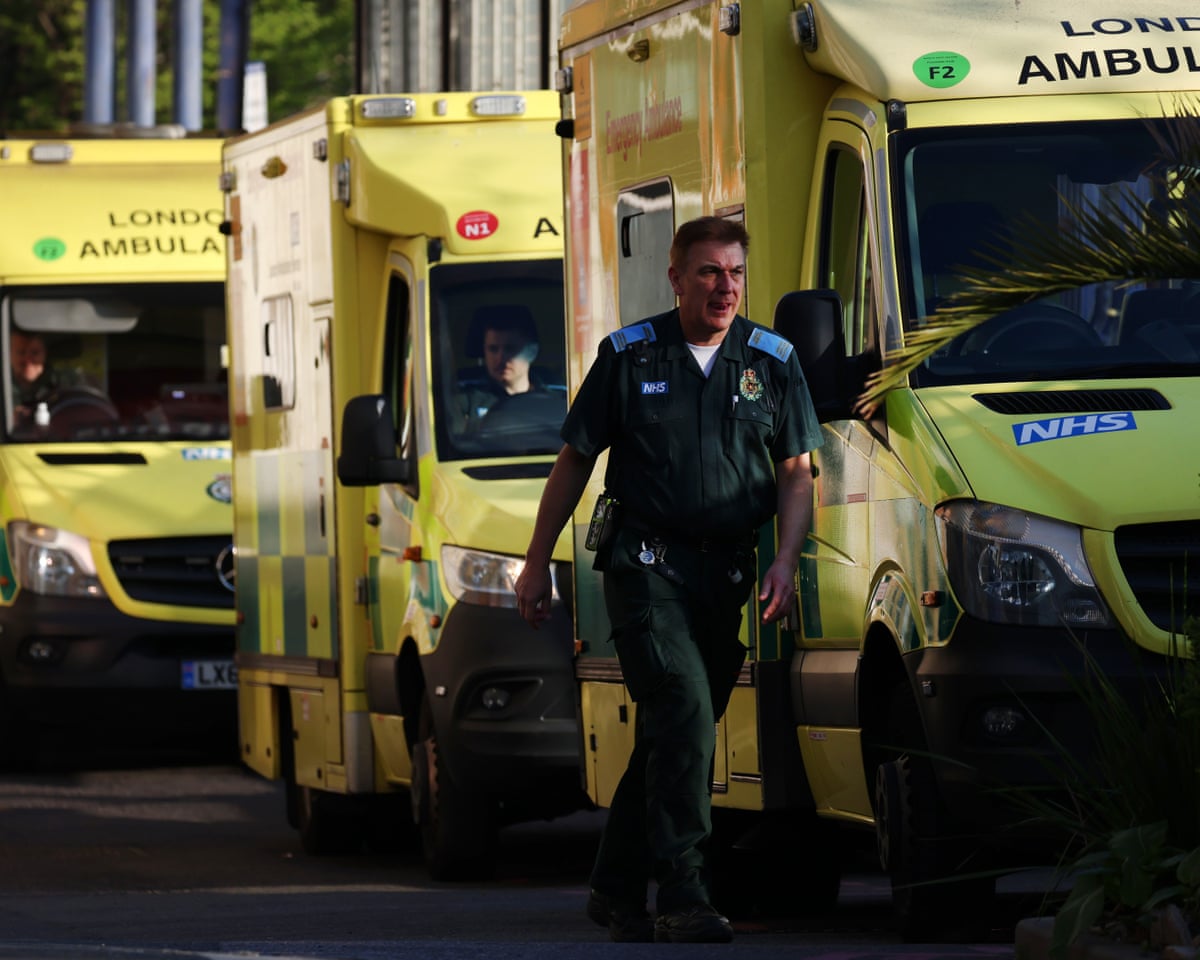 Photo: theukpulse.co.uk An NHS ambulance worker walks past parked yellow London Ambulance vehicles