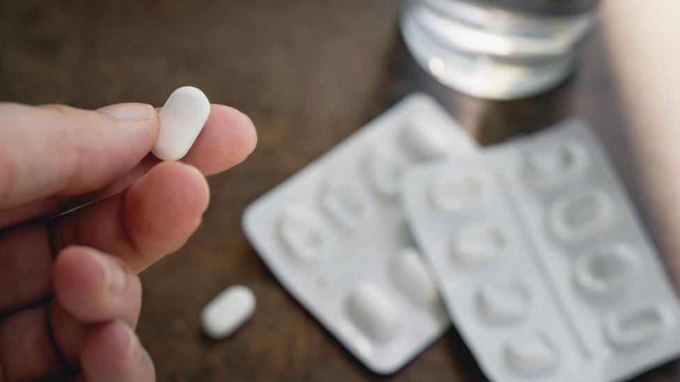 A person holds a paracetamol tablet with the pack and a glass of water blurred in the front of her.