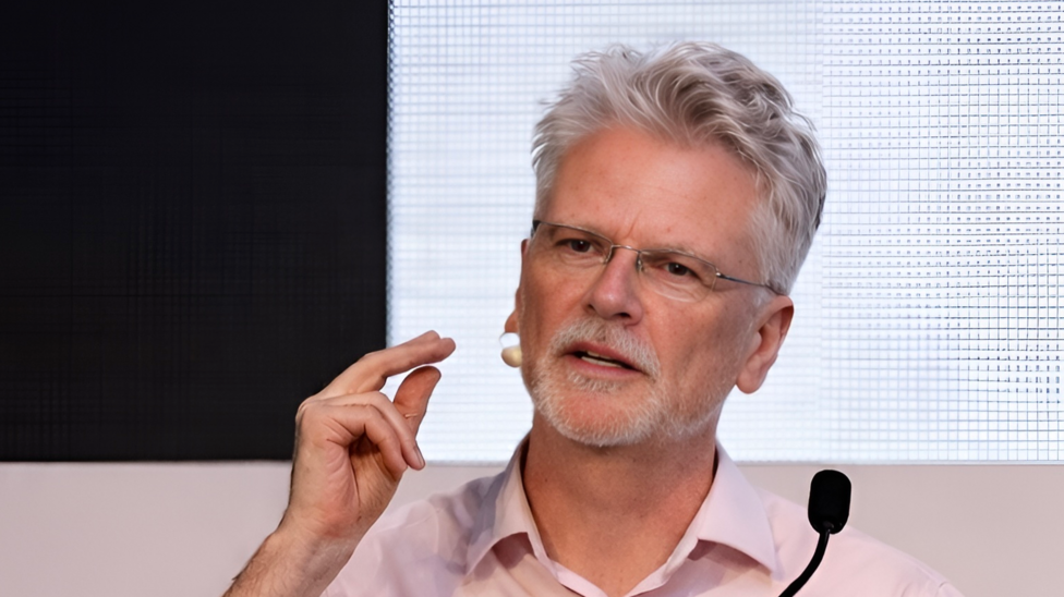 With short grey hair and a grey beard, Peter O'Brien addresses a conference