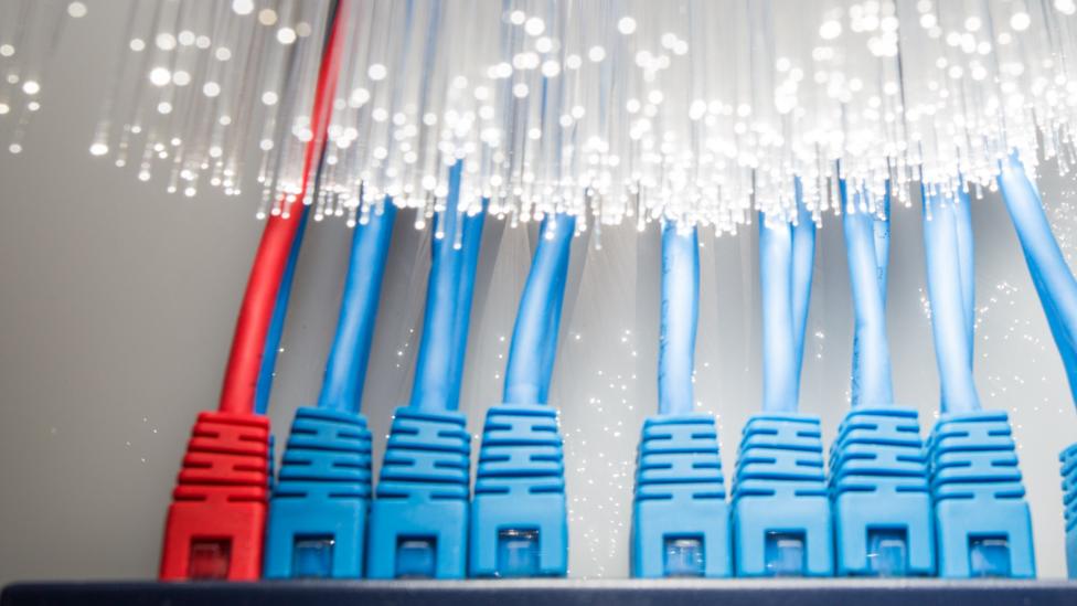 Fibre optic cables give off light next to regular network cables.