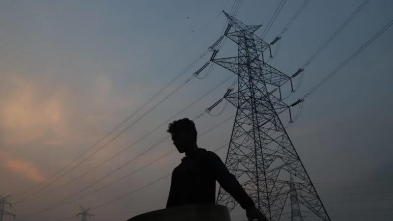 Transmission lines are seen through a filed on the outskirts of Srinagar city with a man in silhouette in the foreground