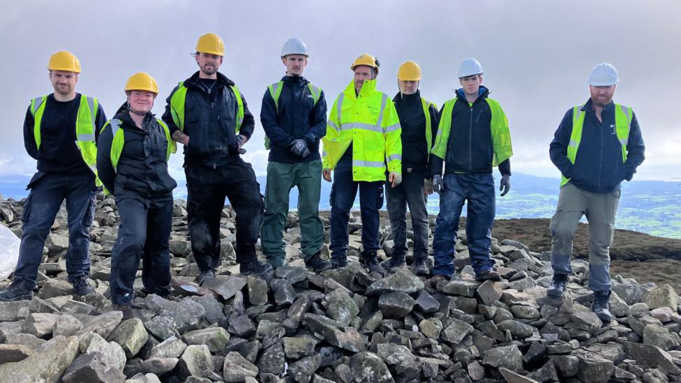 A group of men dressed in high vis jackets stand on rocks