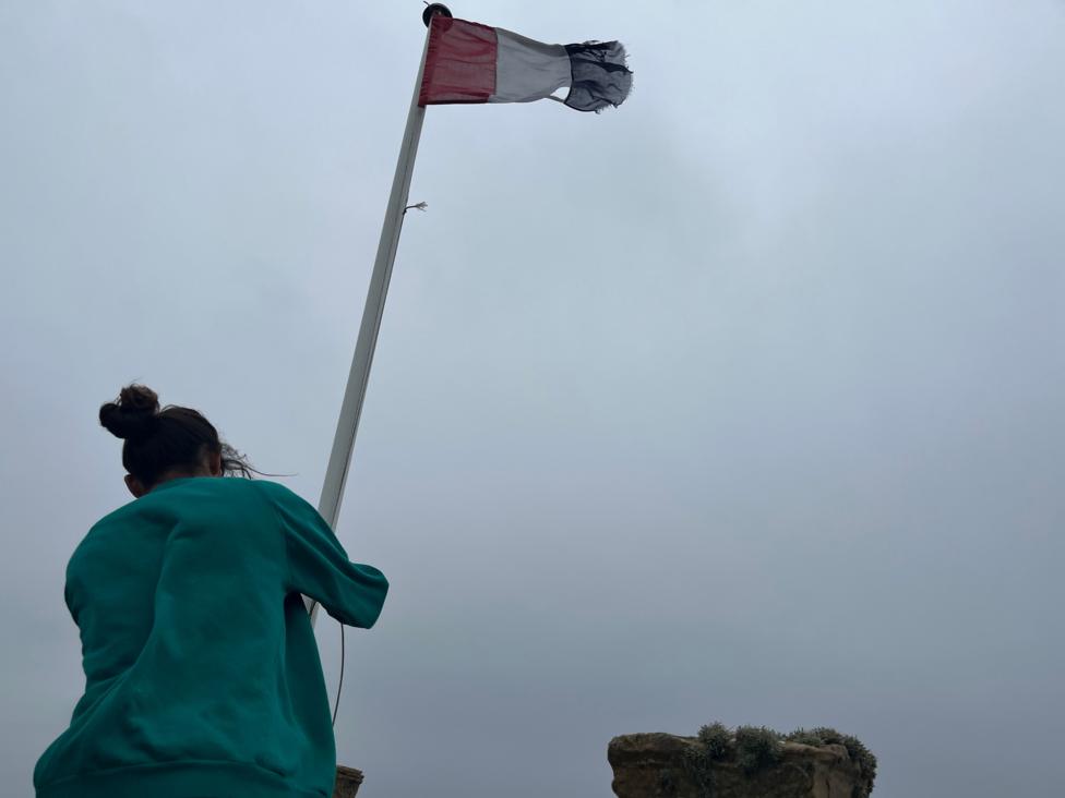 Dad Jorge Suarez raising a flag. He is wearing a green jumper. The sky is grey.