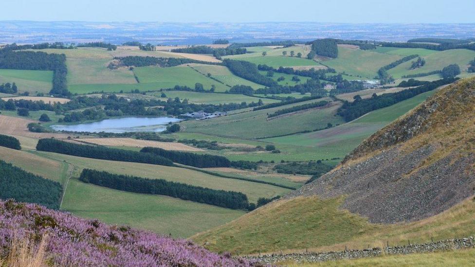A view from hills over the countryside with rolling hills and a small loch