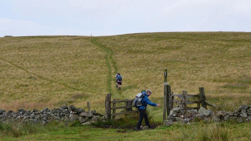 Walkers going through a dry stane dyke and gate head up into the hills