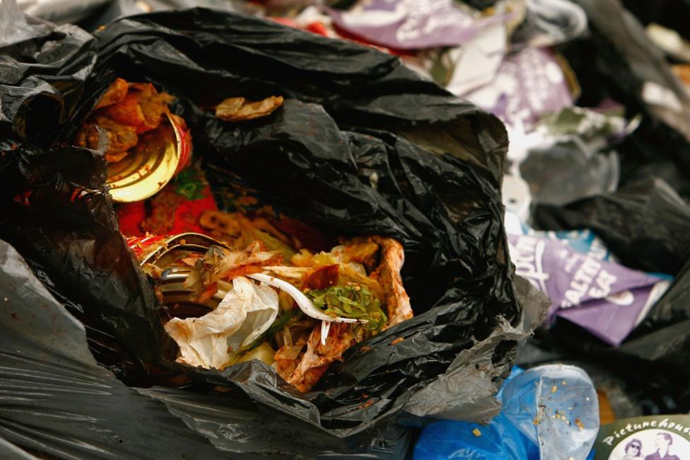 An open black bag containing litter including cans and food waste.