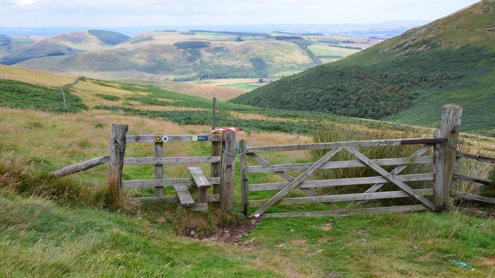 A fence and style on the hills of Northumberland with rolling hills in the distance