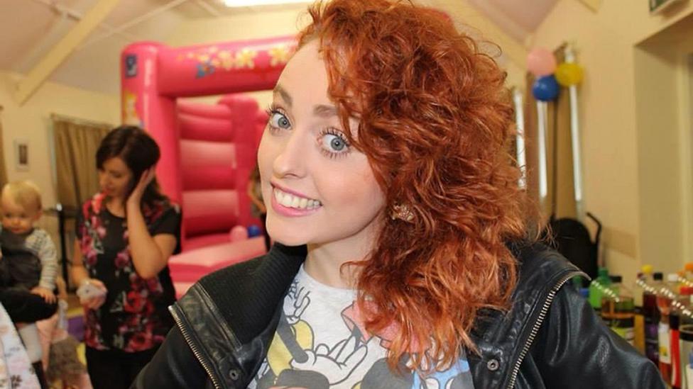 A girl is pictured smiling at the camera, with a bouncy castle in the background.