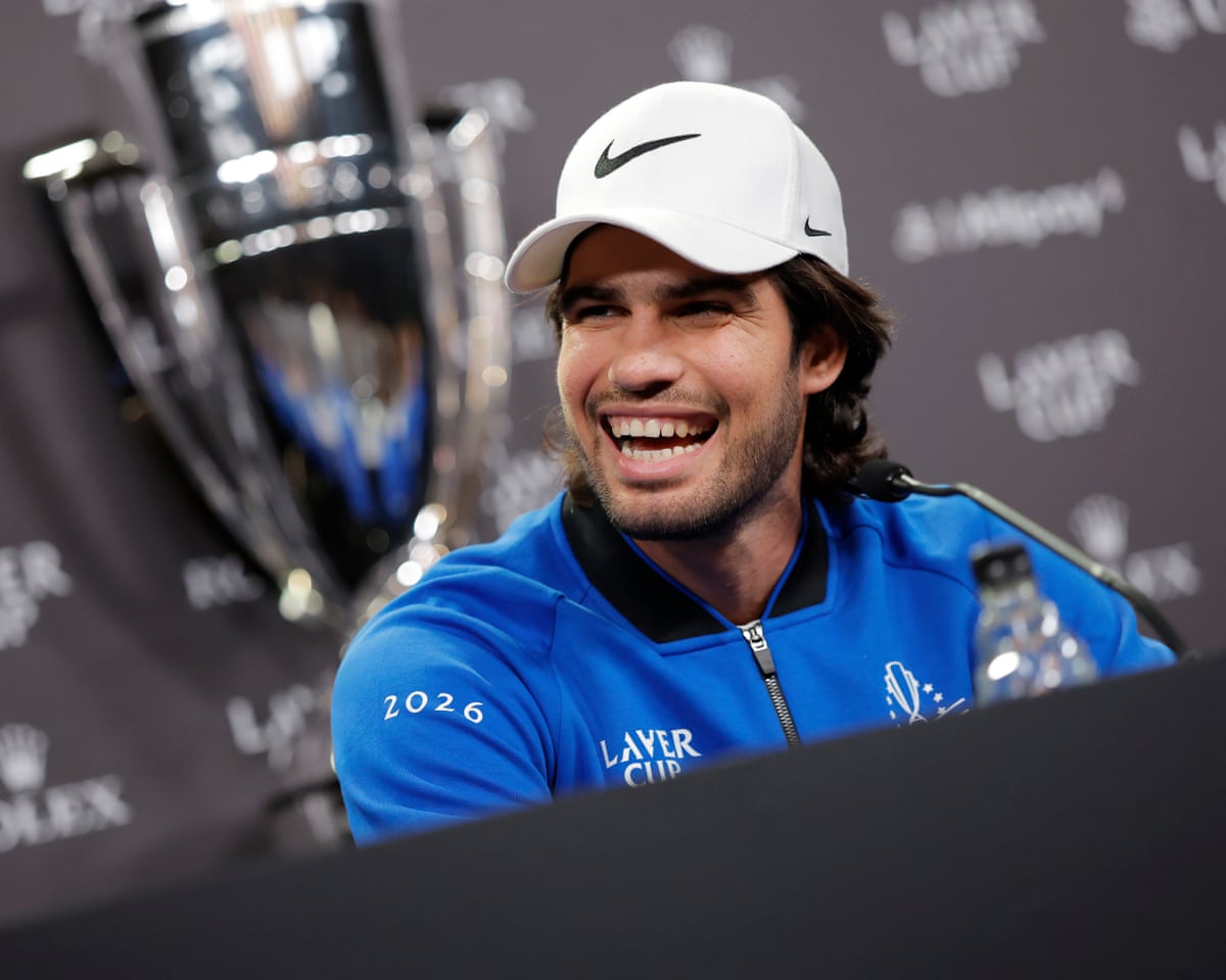 Photo: theukpulse.co.uk Carlos Alcaraz, wearing a Laver Cup branded jacket and a Nike hat and sitting in front of the trophy, laughs during a press
