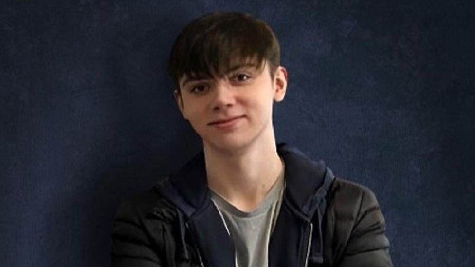 Samuel Whitaker seen on a blue backdrop wearing a grey top, dark hoodie and jacket.