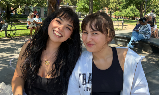 Two women sit on a park bench and smile at the camera