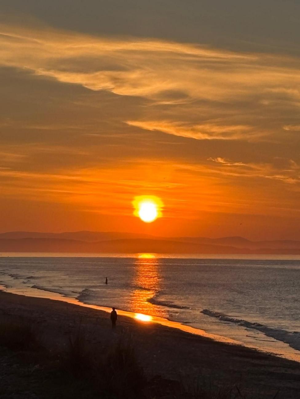Sunset over a beach, with golden light reflecting across the sea and shoreline.