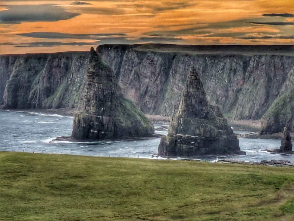 Sea stacks rise from the shoreline beneath towering cliffs at sunset.