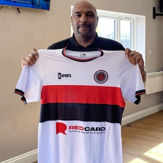 A man holds a white, red and black striped football shirt reading "Red Card" with a slogan underneath.