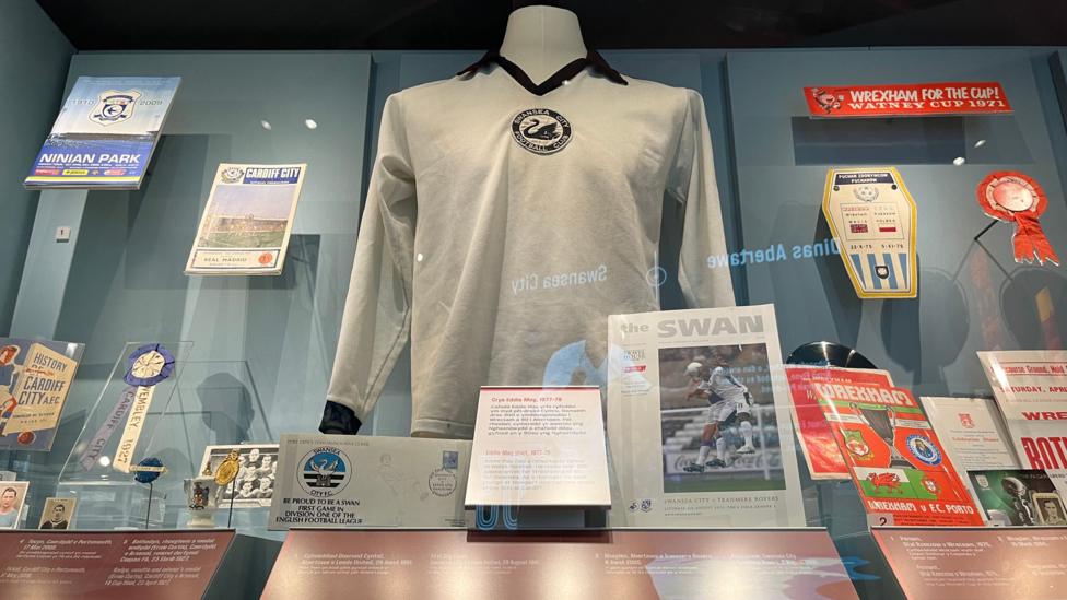 A white football long-sleeved shirt on display. It was a Swansea football logo at the centre of the shirt.