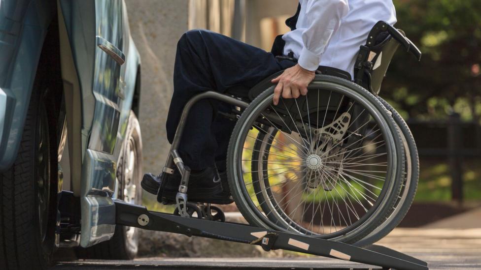 A man in a wheelchair goes up a ramp into the side of a vehicle