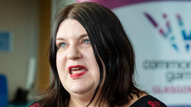 Susan Aitken has shoulder-length dark brown hair. She has blue eyes and is mid-speech