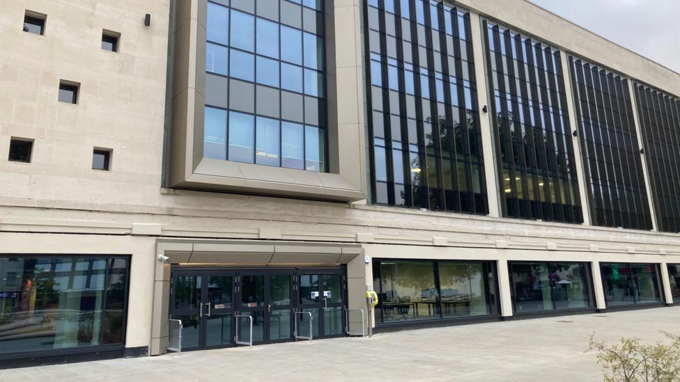 Exterior view of the newly redeveloped former Debenhams building in Gloucester, with a light modern façade, large windows and paved pedestrian area in front. 