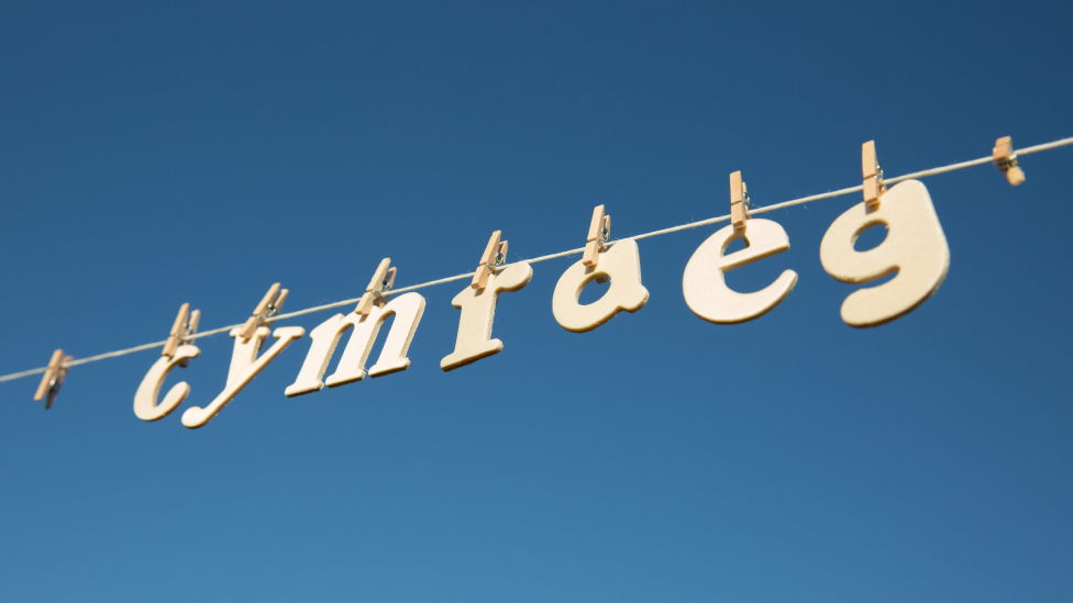 Cymraeg spelt out on a clothesline with pegs holding letters in front of a blue sky