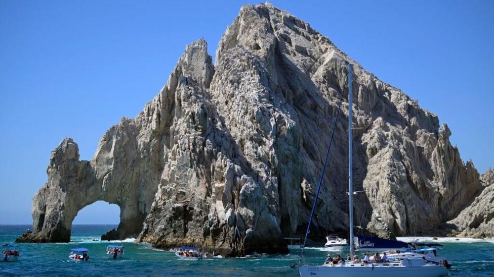 View of the rock formation called "The Arch" in Los Cabos, Baja California state, Mexico on February 21, 2024. The rock formation is photographed against a deep blue sky and in the turquoise waters small boats carrying tourists can be seen criss-crossing the waters around the arch.