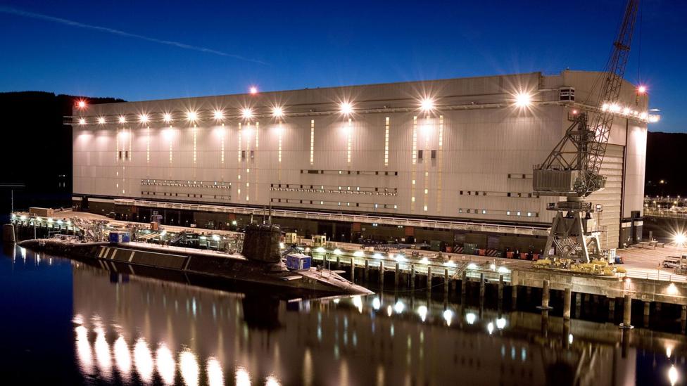 A large white building, lit up at dusk with a submarine in the foreground
