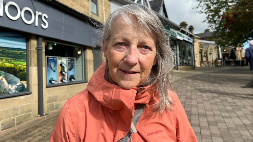 A woman with grey hair wears a salmon coat.