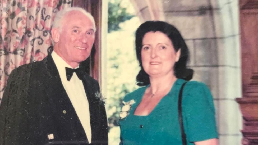 John and Teresa Russell are pictured at a function. John is wearing a black jacket, white shirt with a bow tie. Teresa is wearing a green dress.