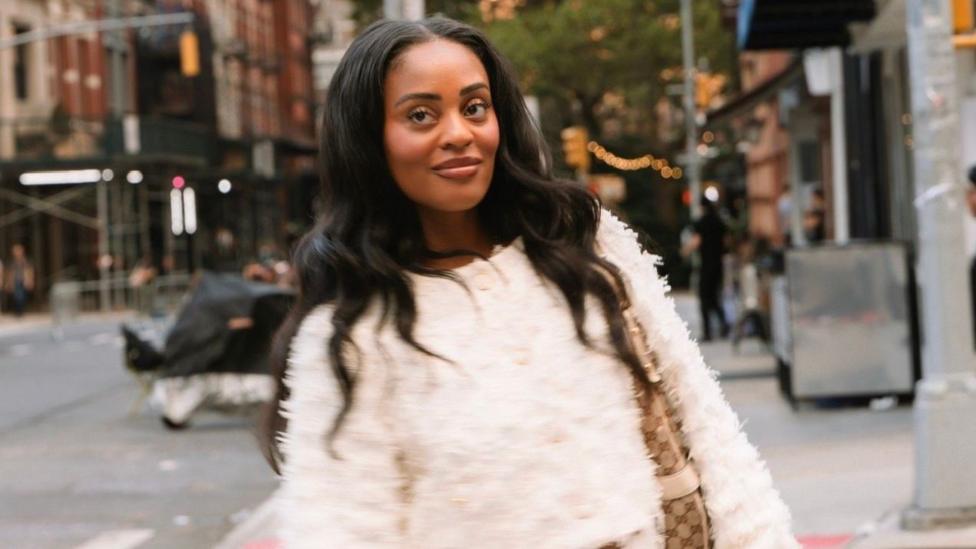 Aiesha Beasley stands in a city street while wearing a fury cream-coloured jumper