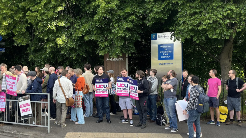A line of students holding placards next to a University of Nottingham sign