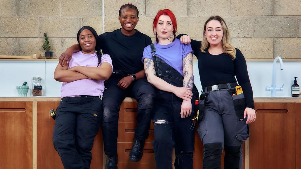 Four TaskHer tradeswomen smiling as they sit or lean against a kitchen worktop.