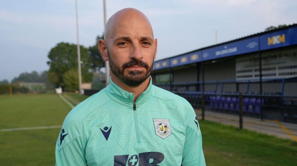 A man with a beard and white sports top looks directly at the camera