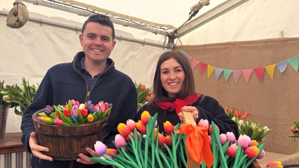 A man and a woman smiling at the camera while holding tulips in a basket.