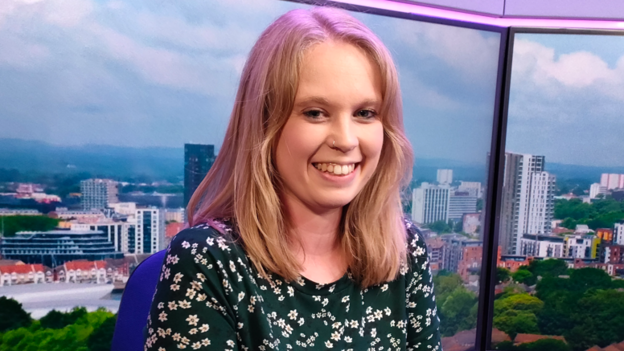 Natalie Parker, a woman with long blonde hair, smiles at the camera in a radio studio. She is wearing a floral top.