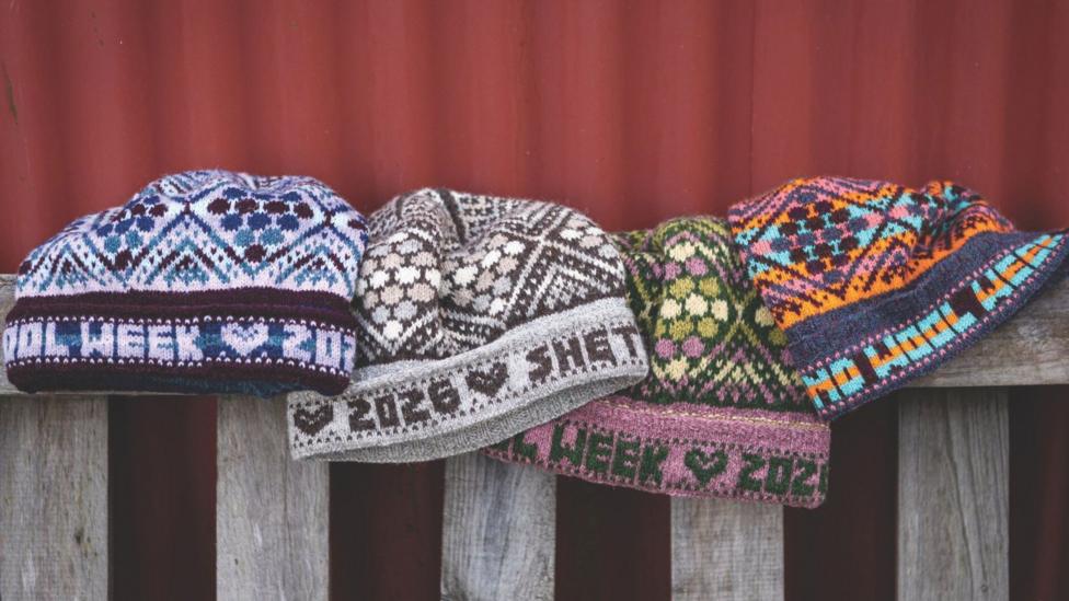 Four Birsie Beanny hats of different colours are posed on top of the back of a wooden bench.
