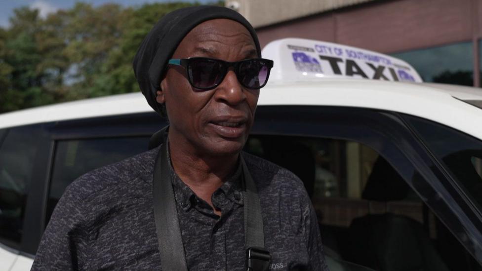 Southampton taxi driver Neil McLean stood in front of a cab. He is wearing sunglasses, a hat and a dark t-shirt.