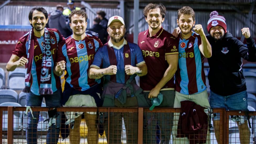 A group of Trabzonspor fans pose for the camera pitch-side at Drogheda's stadium.