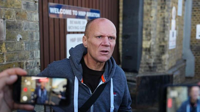 A middle-aged man in a hoody stood outside next to a brick wall.