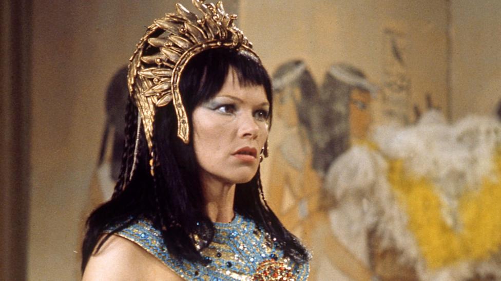 Glenda Jackson in a black wig with a fringe, gold headdress and jewelled outfit as Cleopatra