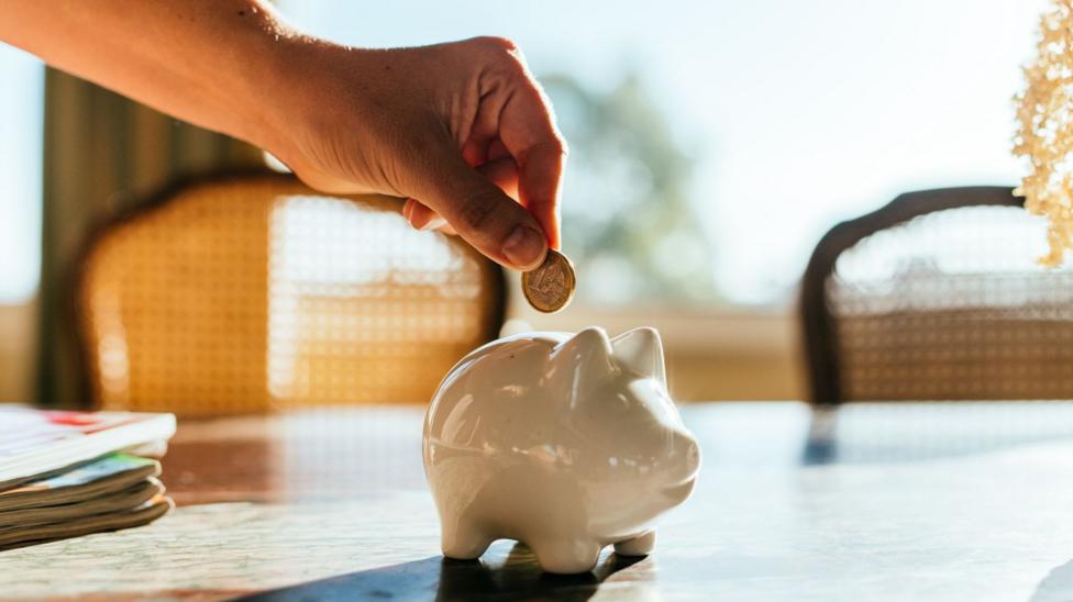 A hand puts pound coin into a white piggy bank.
