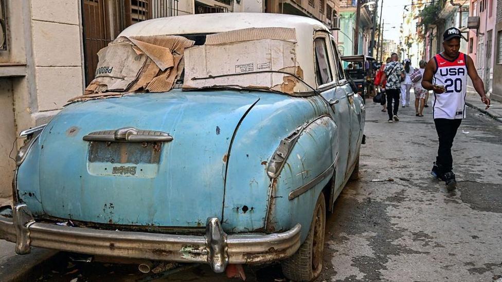 A man walks past an old car on a street in central Havana