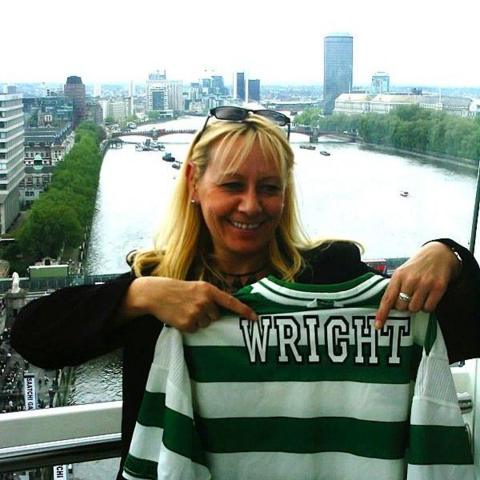 A blonde woman stands inside a London Eye capsule holding up a green-and-white striped football shirt with the name “WRIGHT” on the back. Through the glass, the River Thames and central London skyline stretch into the distance, creating a striking city backdrop.