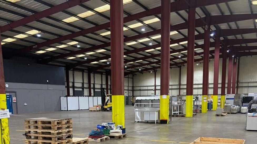 Inside a factory with large empty spaces, pillars and some pallets